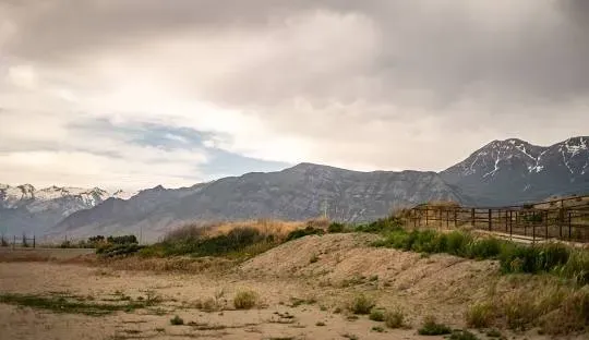 Mountains and plains under a cloudy sky, with a wooden fence on a ridge.
