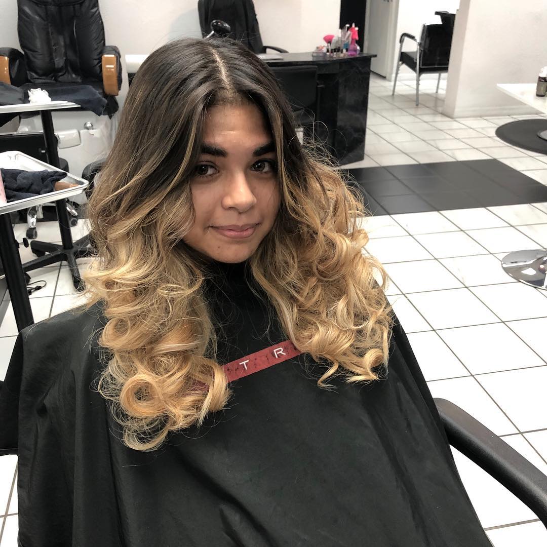 A woman in a black cape is sitting in a chair in a salon.