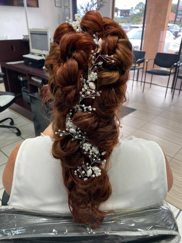 A woman is sitting in a chair with her hair in a braid and flowers in her hair.