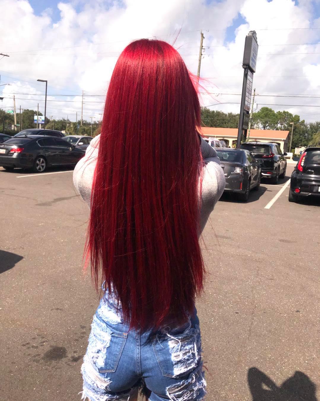 A woman with long red hair is standing in a parking lot.
