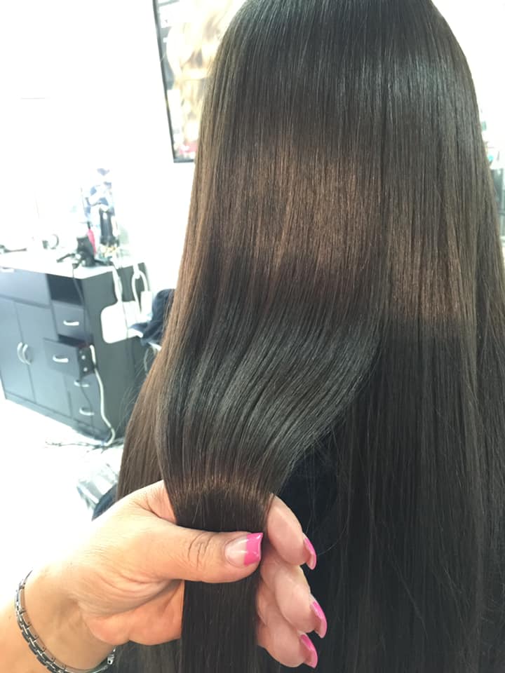 A woman with pink nails is holding her hair in a salon.