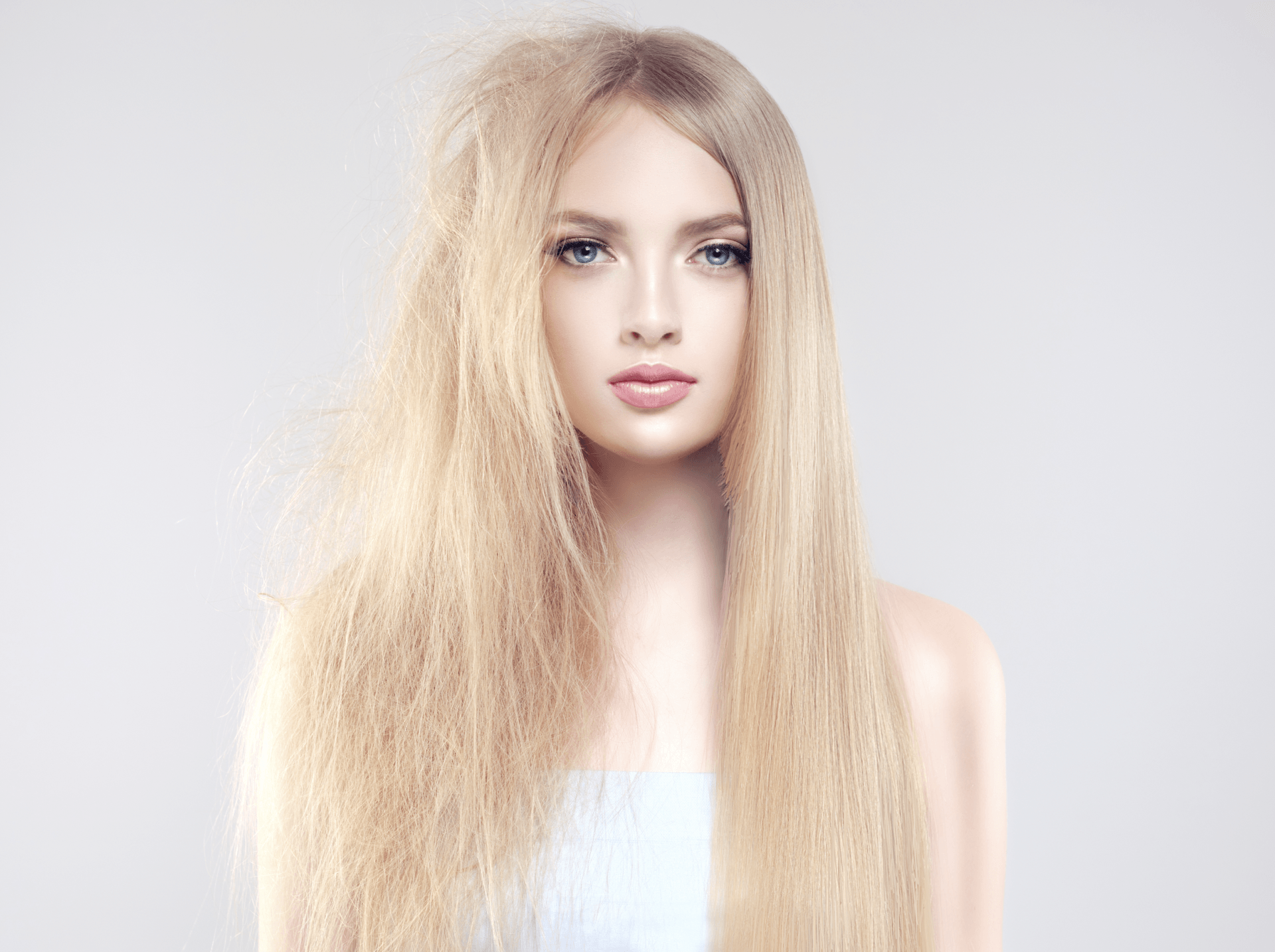 A woman with long blonde hair is standing in front of a white background.