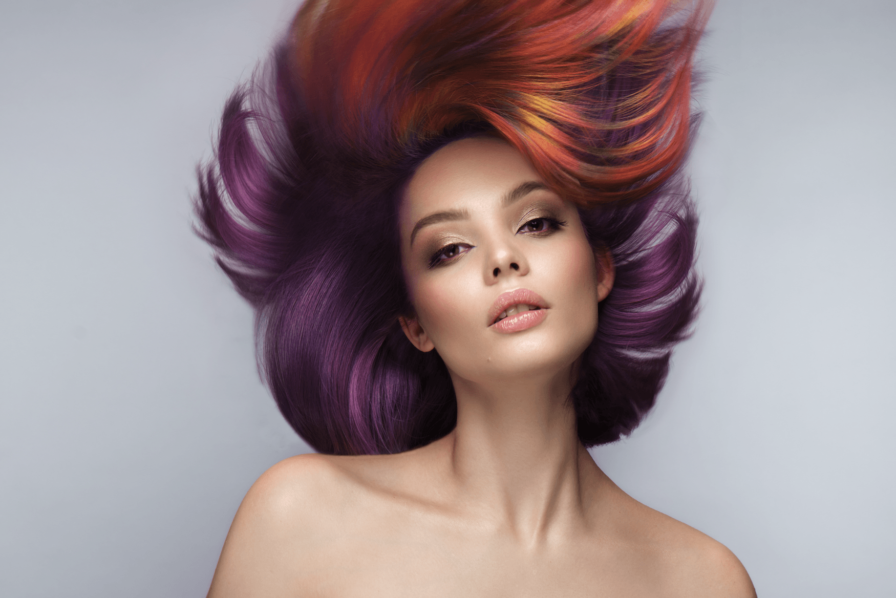 A woman with red and purple hair is laying down with her hair blowing in the wind.