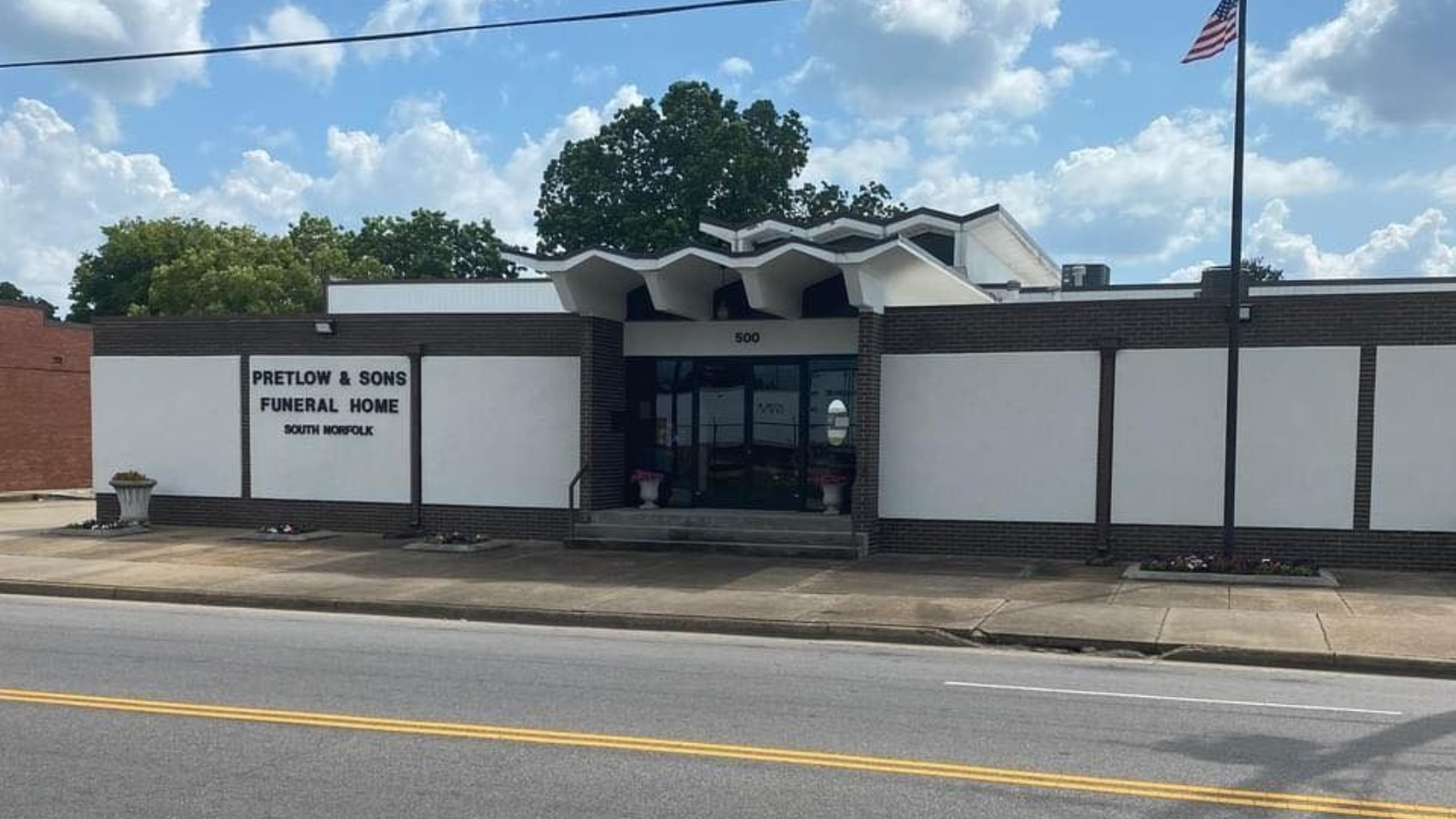 Funeral home with brick facade, white walls, arched entryway, and American flag.