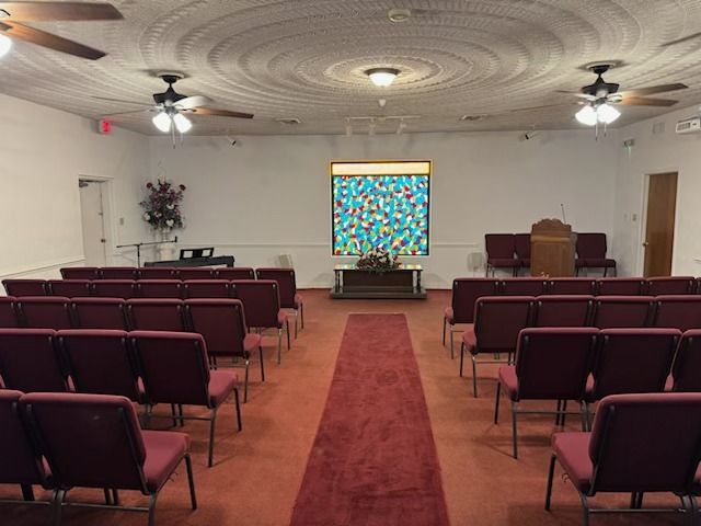 Rows of burgundy chairs face a stage in a church. A red carpet leads to the altar, with a stained-glass window backdrop.