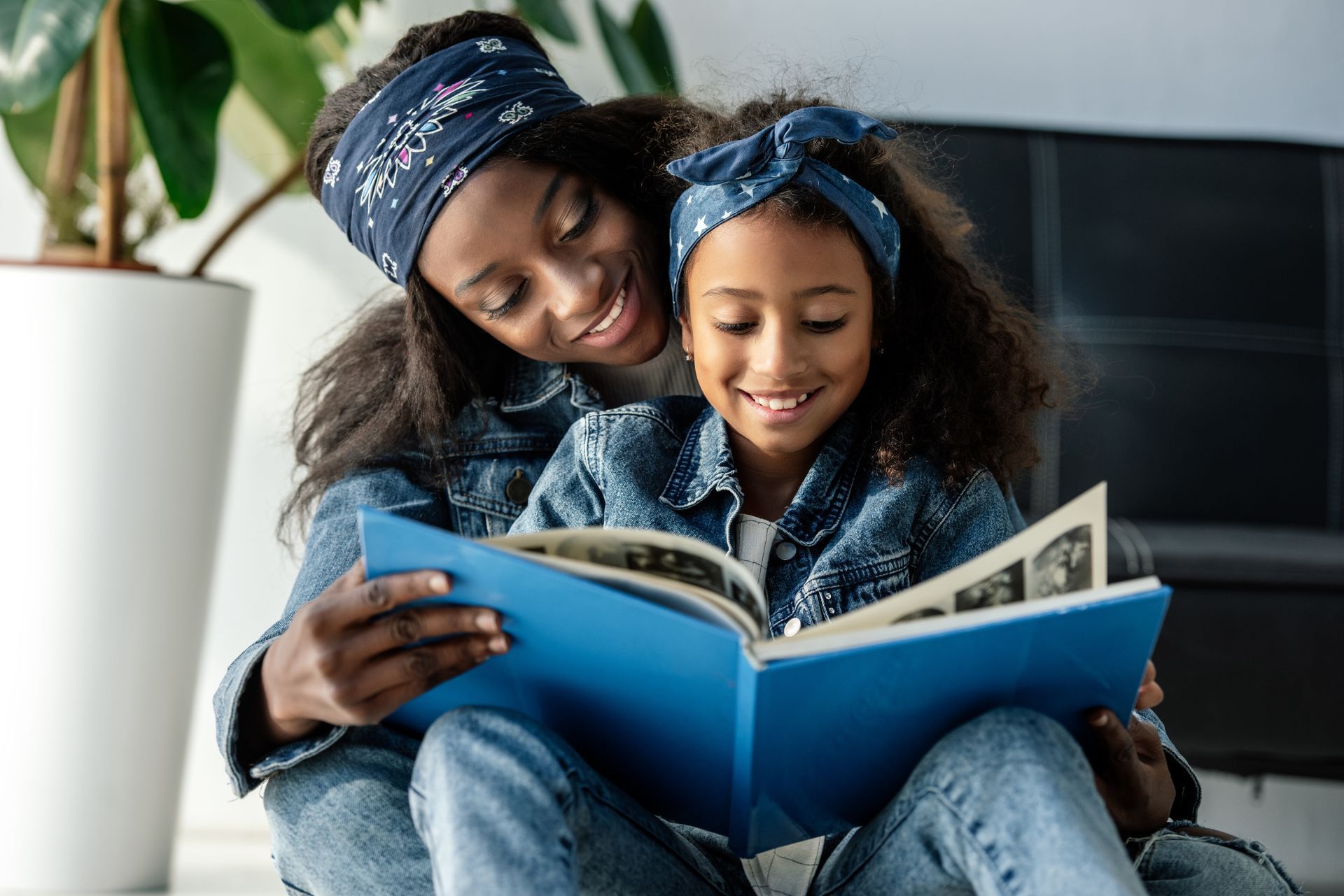 Mother and daughter wearing matching denim outfits and headbands, looking at a photo album together.