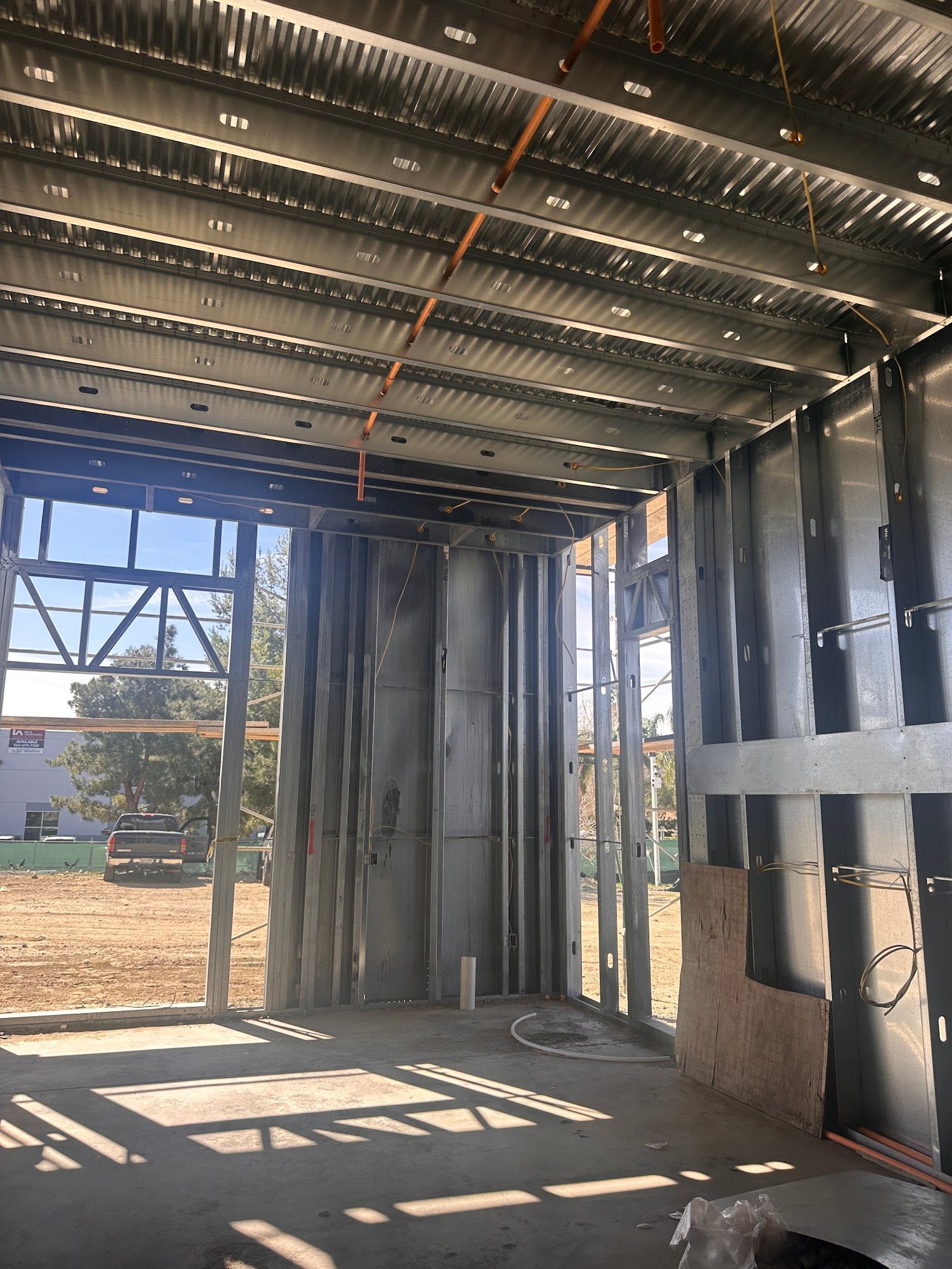 Interior of a building under construction, showing metal framing and exposed ceiling. Exterior view through window.