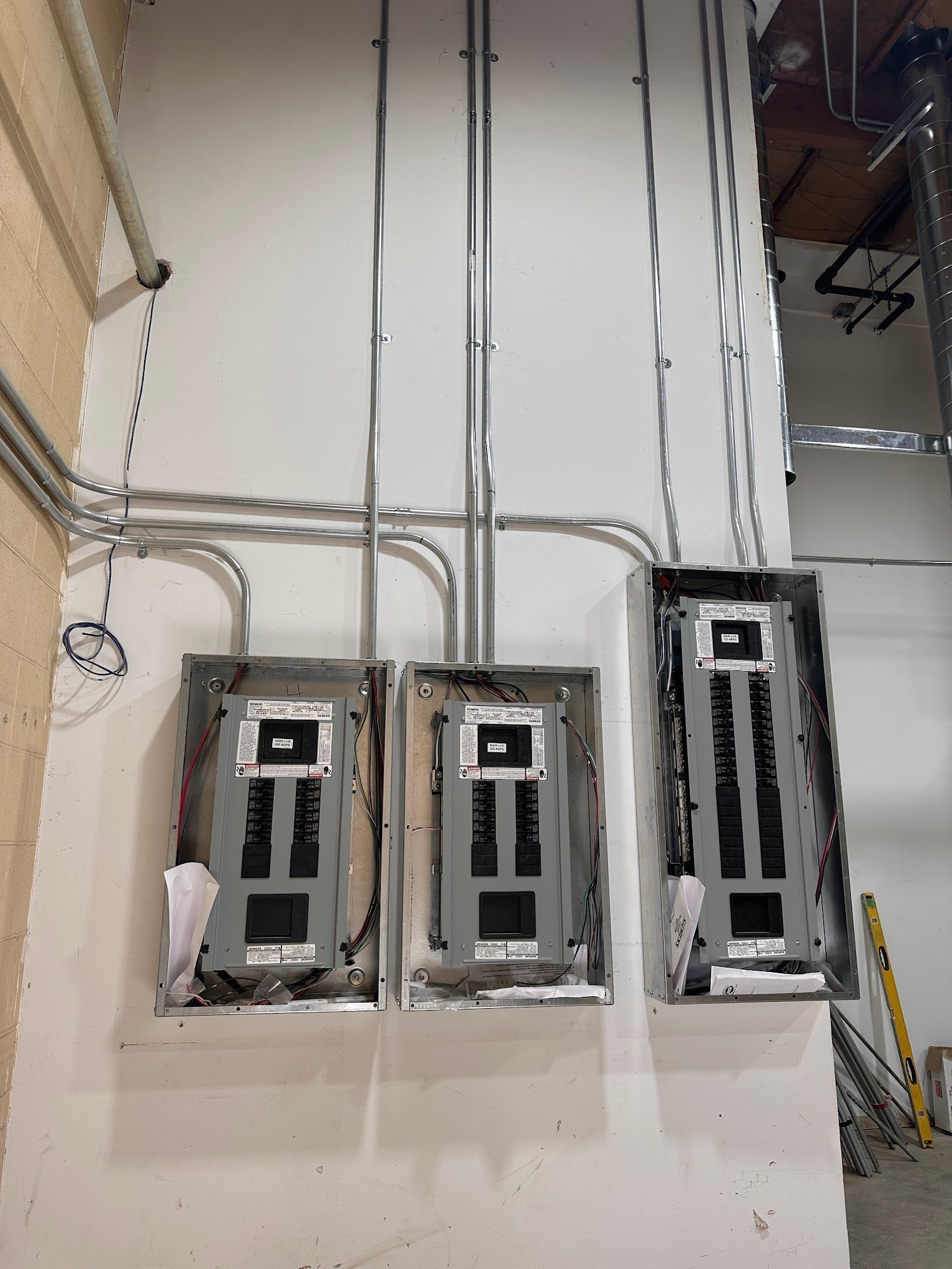 Three electrical panels mounted on a white wall, with conduit running above.