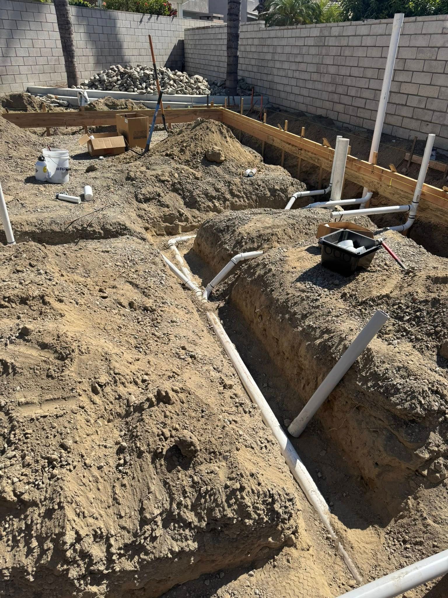 Construction site with trenches, PVC pipes, and exposed ground.