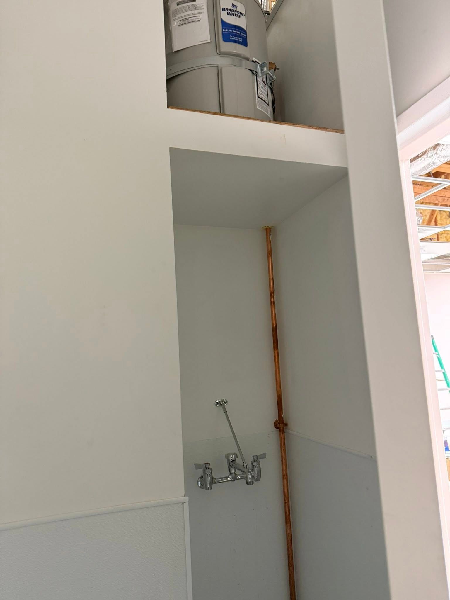 Copper pipes and faucet in white wall alcove, with water heater above.
