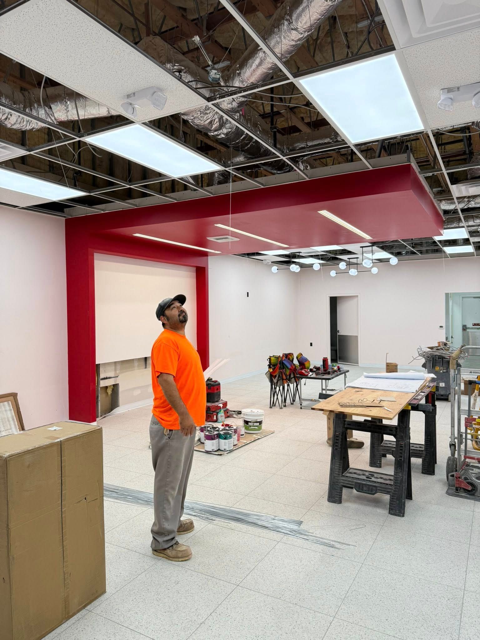 Construction worker looks up at a red and white ceiling installation in a brightly lit room.