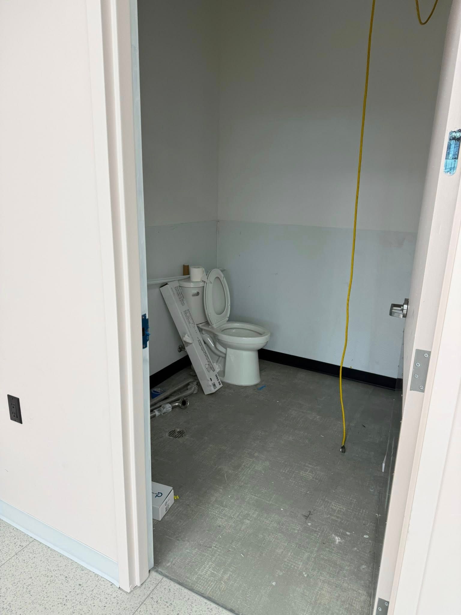 Unfinished bathroom with toilet, exposed wiring, and construction materials on the floor. White walls.