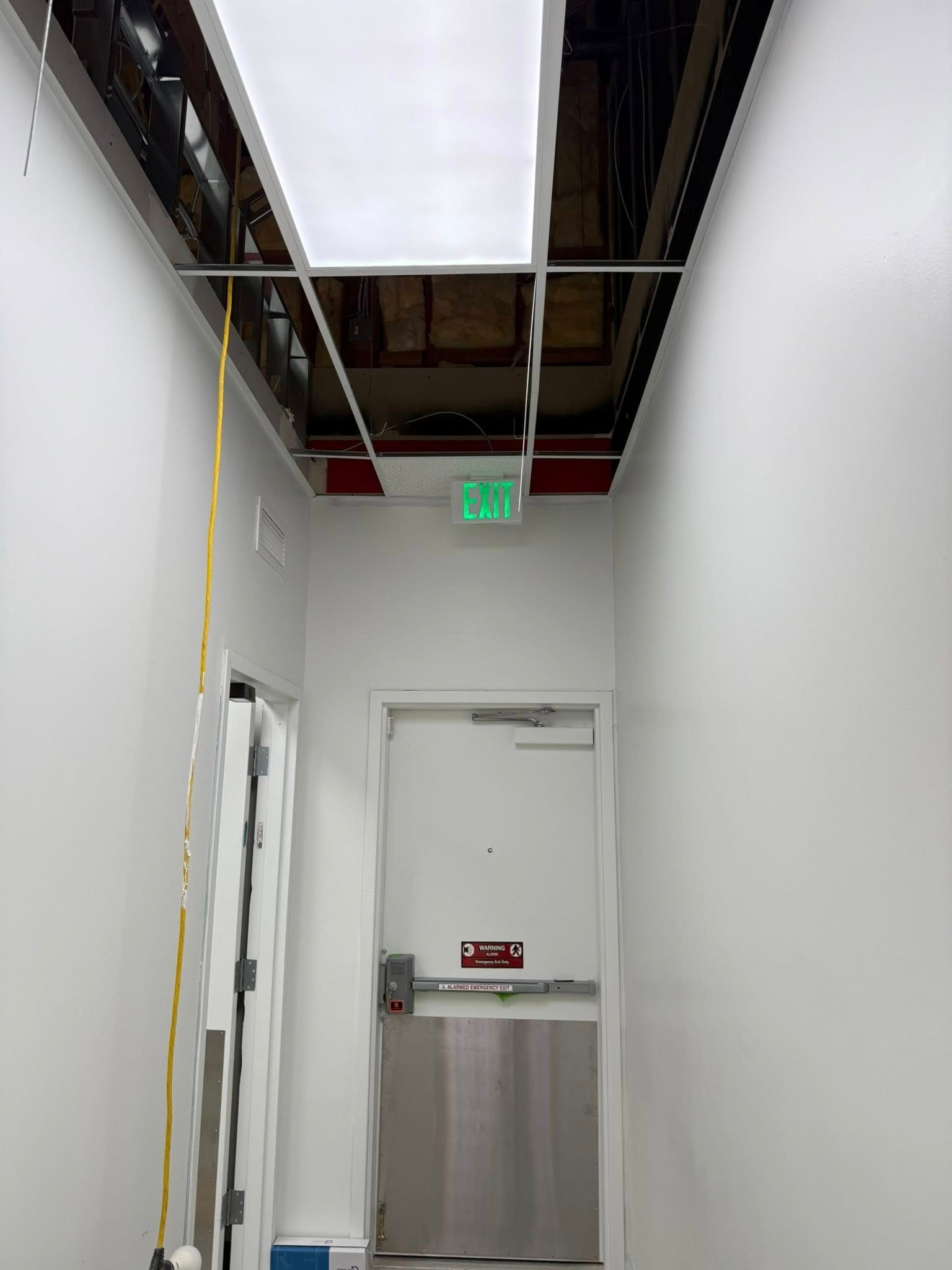 Narrow hallway with an open ceiling, a door, and an exit sign.