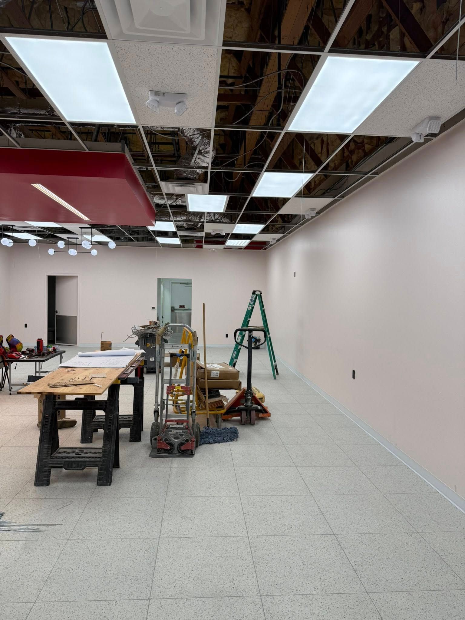 Construction interior with exposed ceiling, pink walls, tools, and a stepladder.