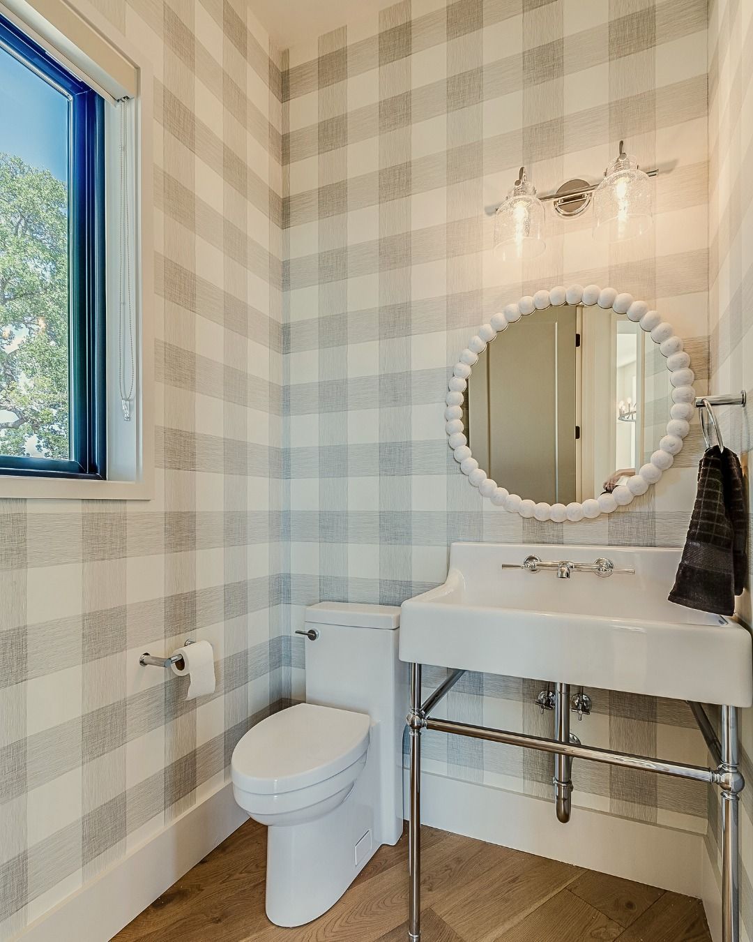 A bathroom with checkered wallpaper, a white sink, and a round mirror.