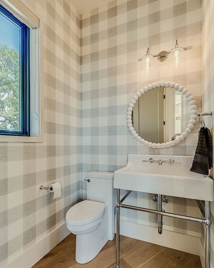 A bathroom with checkered wallpaper, a white sink, and a round mirror.