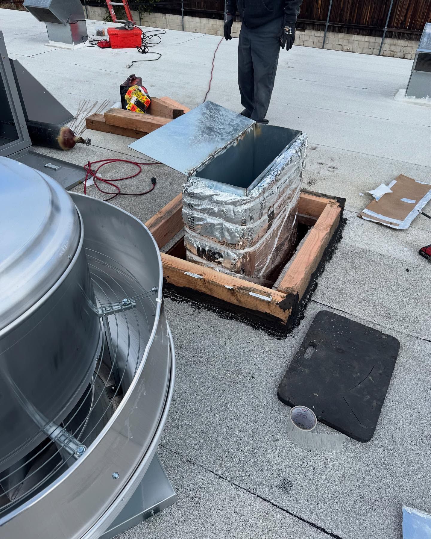 Rooftop work: A worker near ventilation equipment, metal duct, and a roof vent.