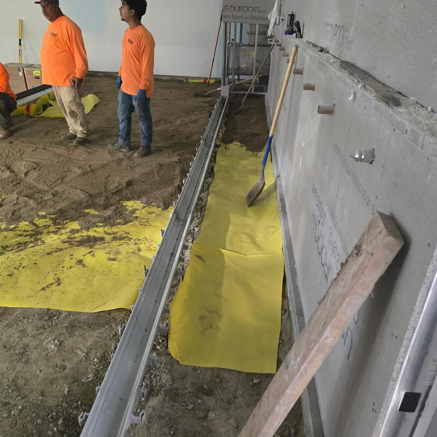 Construction workers preparing a floor for work. Workers in orange shirts stand near a trench covered in yellow fabric.