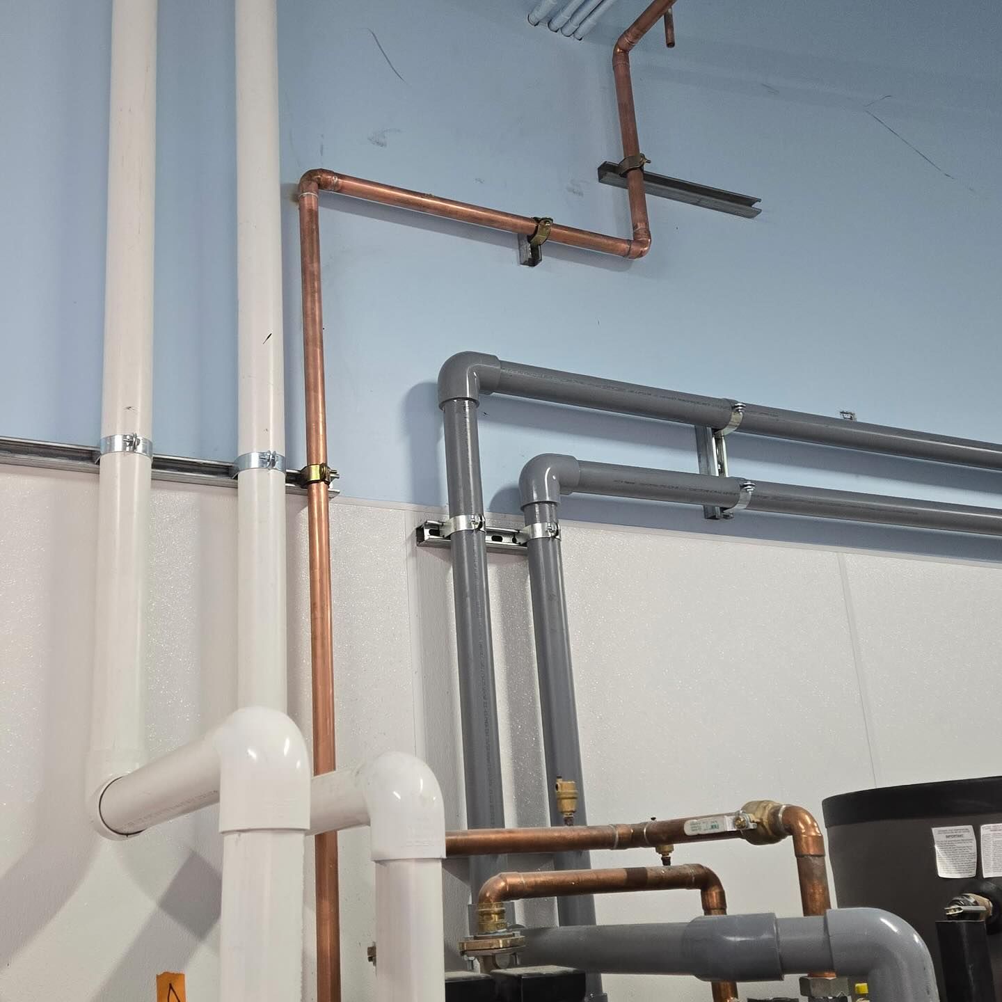 Pipes of various materials and colors run along a white wall, including copper and PVC.