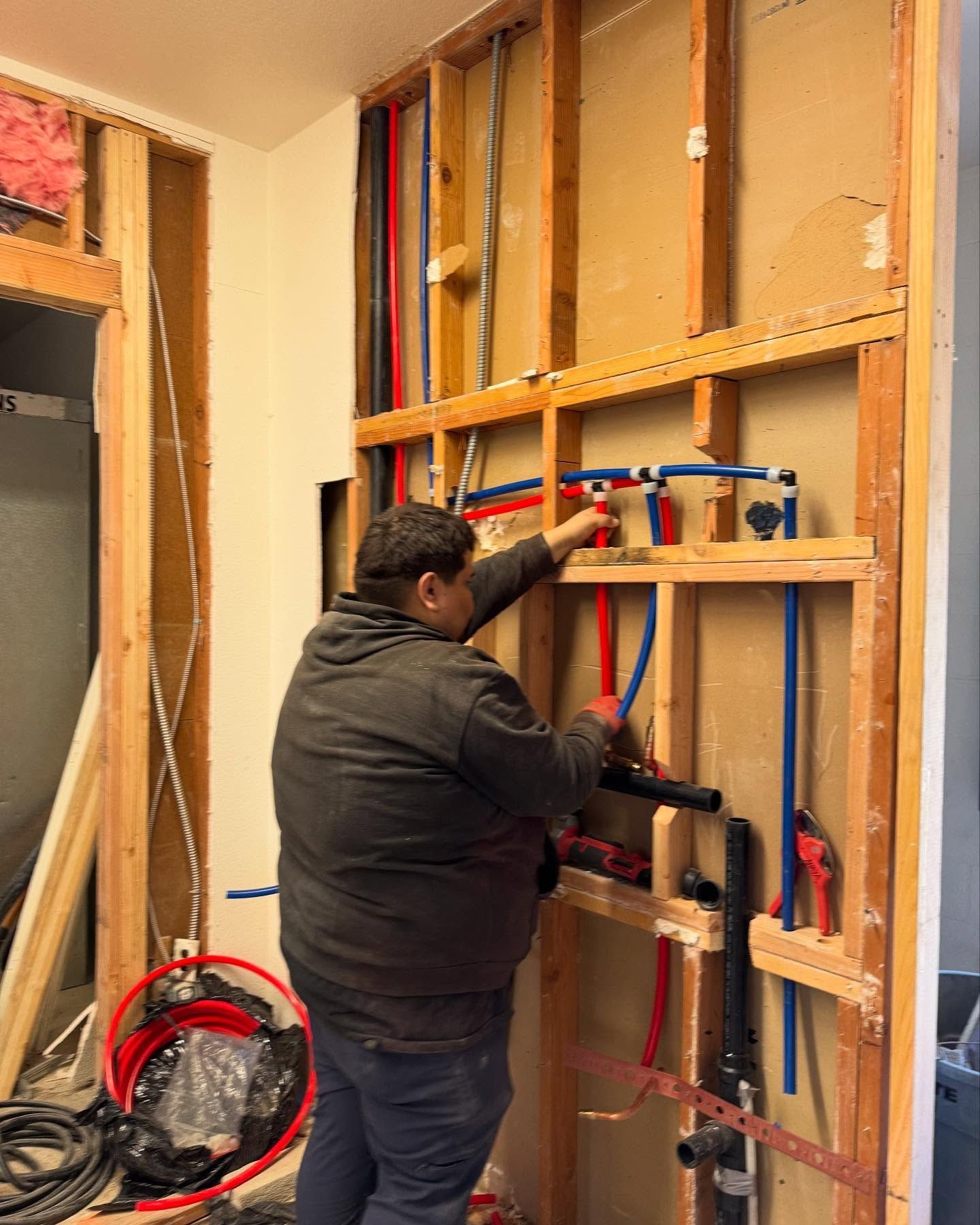 Plumber working on plumbing pipes inside a wall during construction.