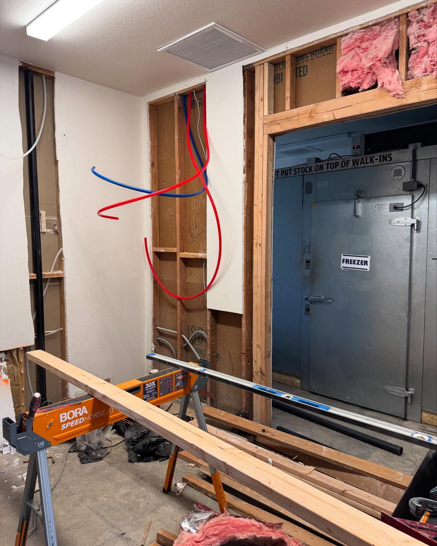 Interior construction site with exposed framing, plumbing, and a large metal door.