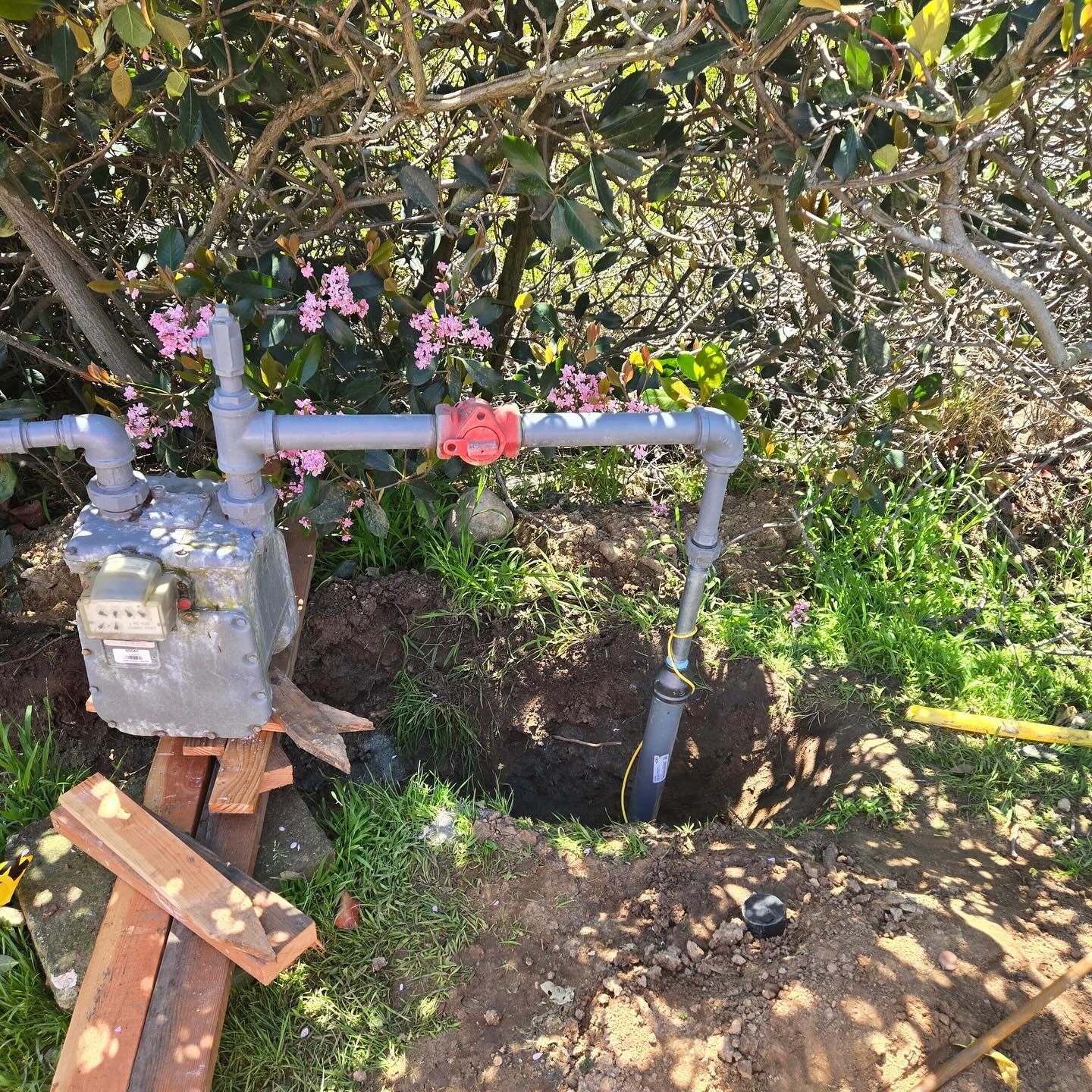 A natural gas meter with exposed piping and a small excavation in a yard.