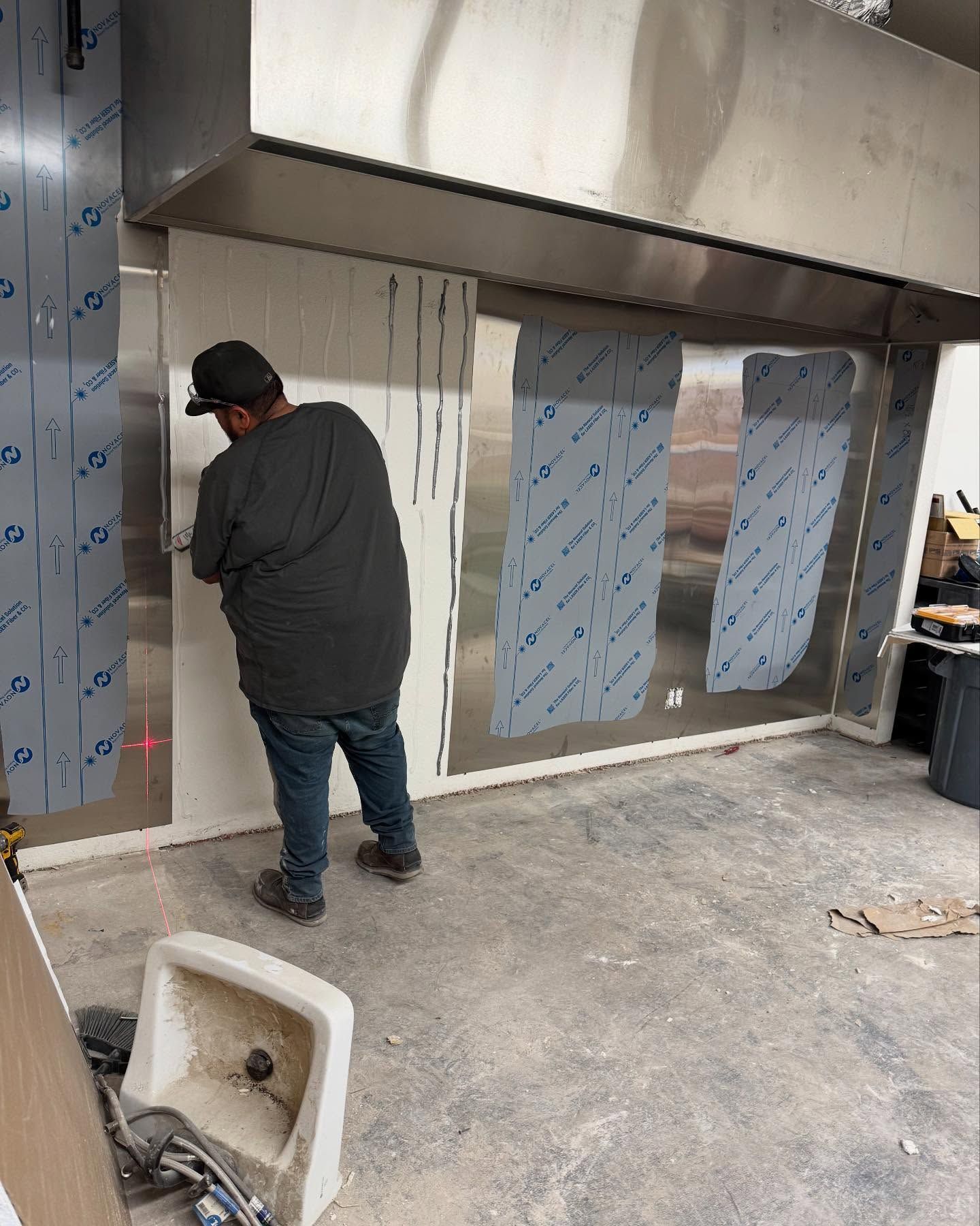 Person installing stainless steel panels under a commercial hood. Construction in progress.