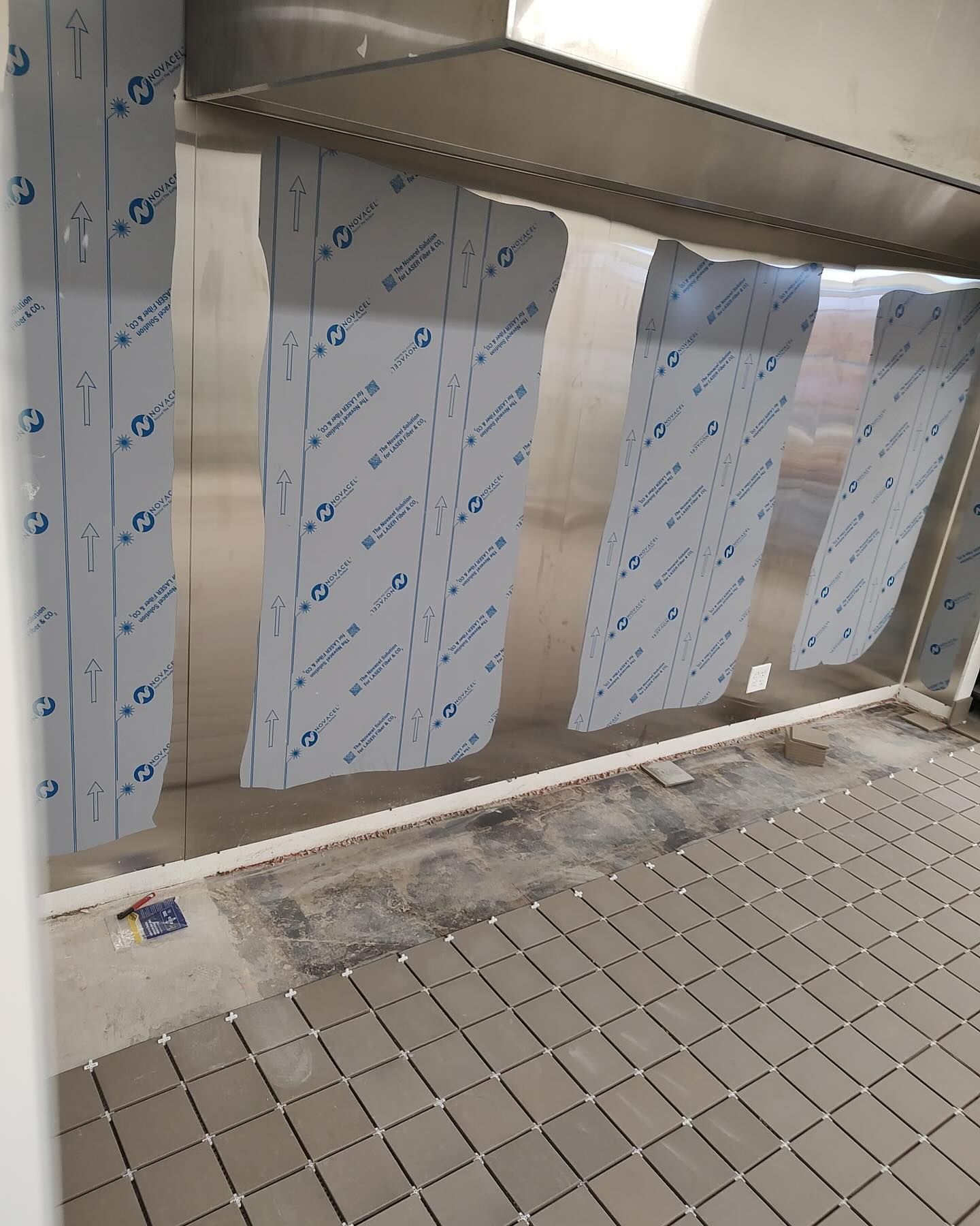 Interior with stainless steel walls covered in protective film, tiled floor, and a metal structure above.