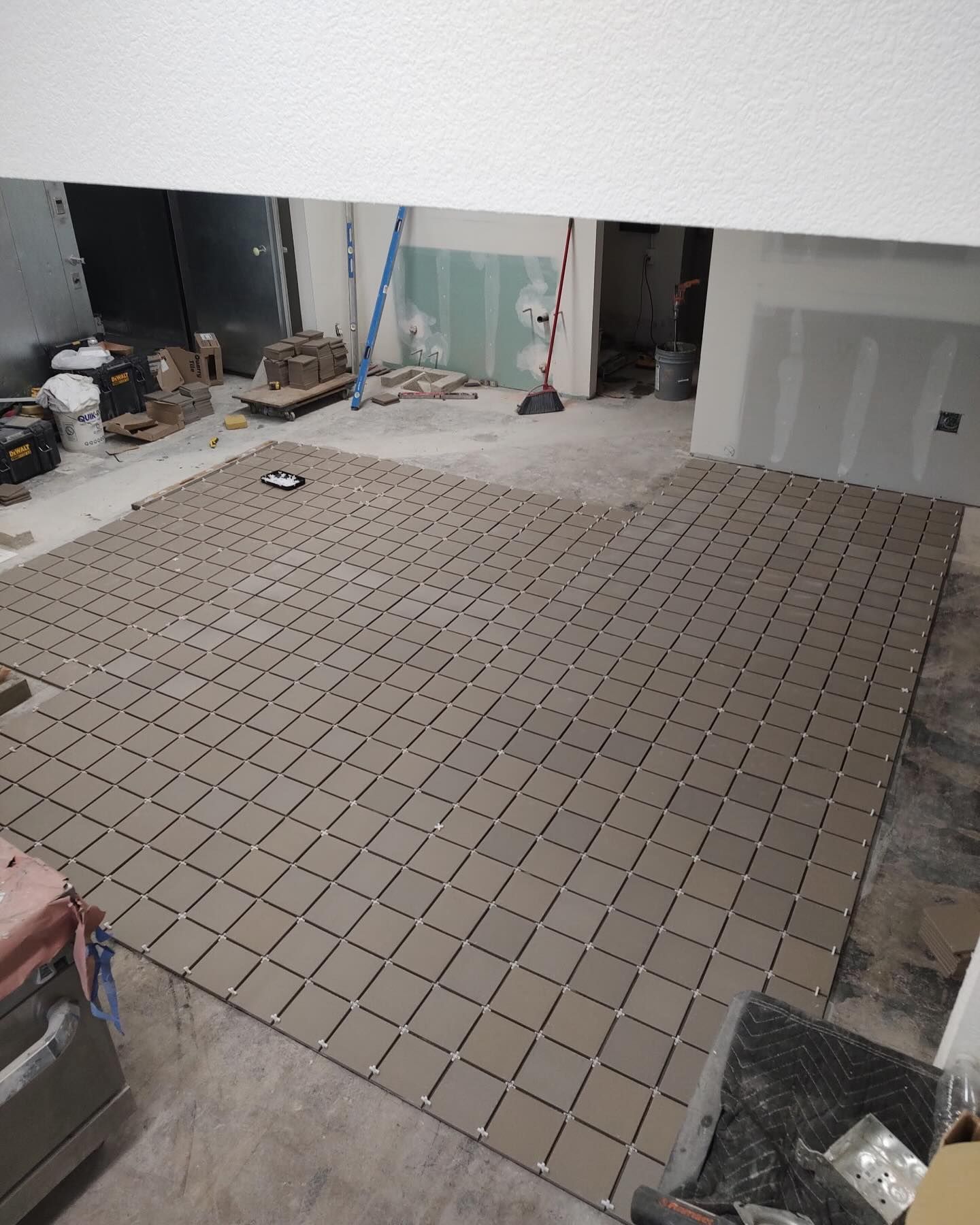 Tile flooring installation in progress. Gray square tiles cover a large area of a room.