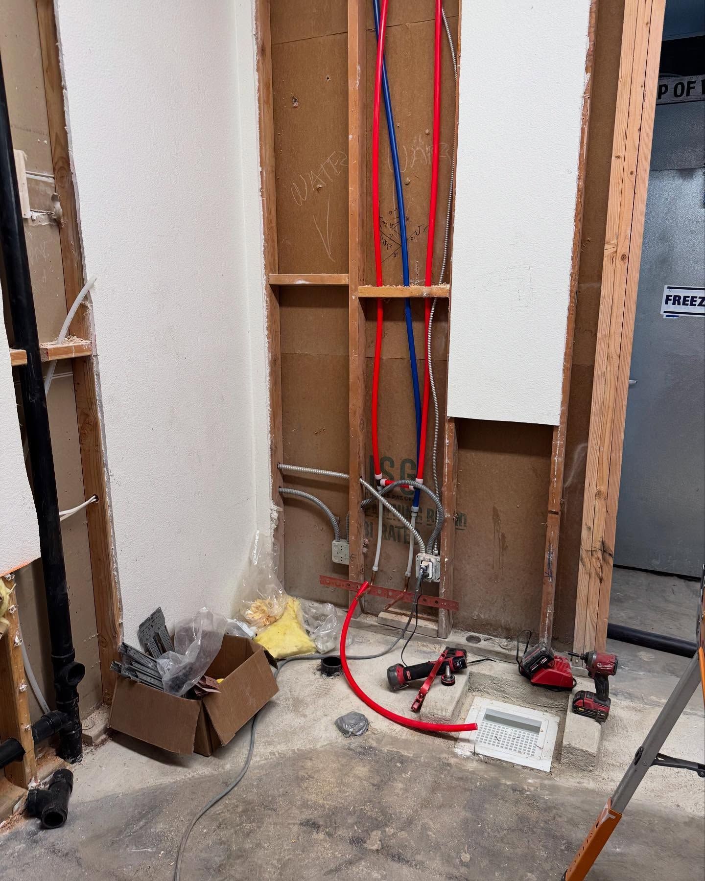 Interior renovation with exposed plumbing and electrical work. Red and blue pipes. Construction tools on the floor.