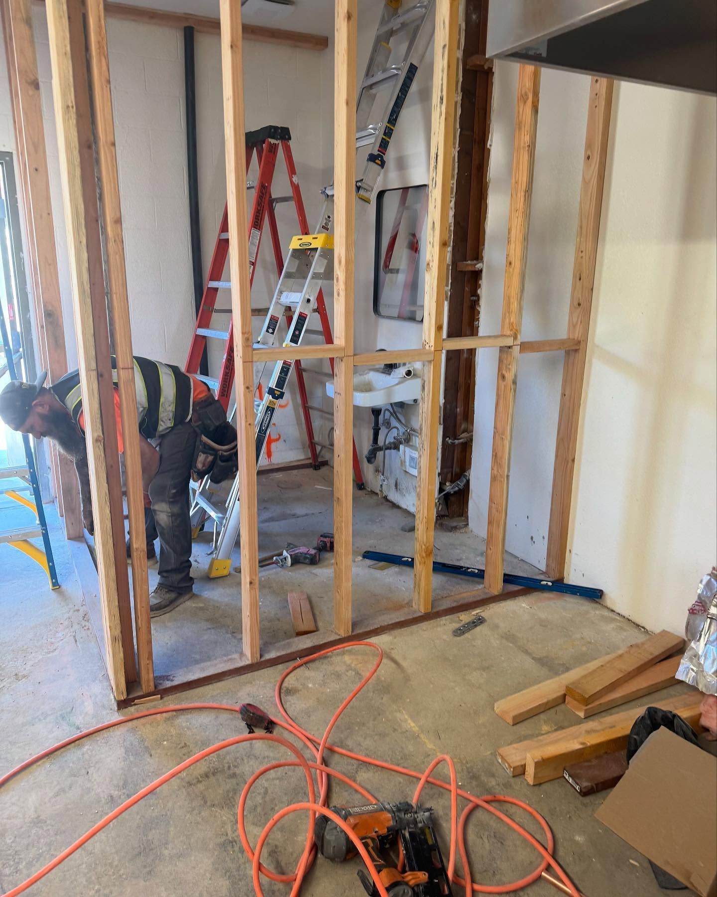 Man framing a wall during a remodel. Interior view, visible studs, ladders, tools, and wires.