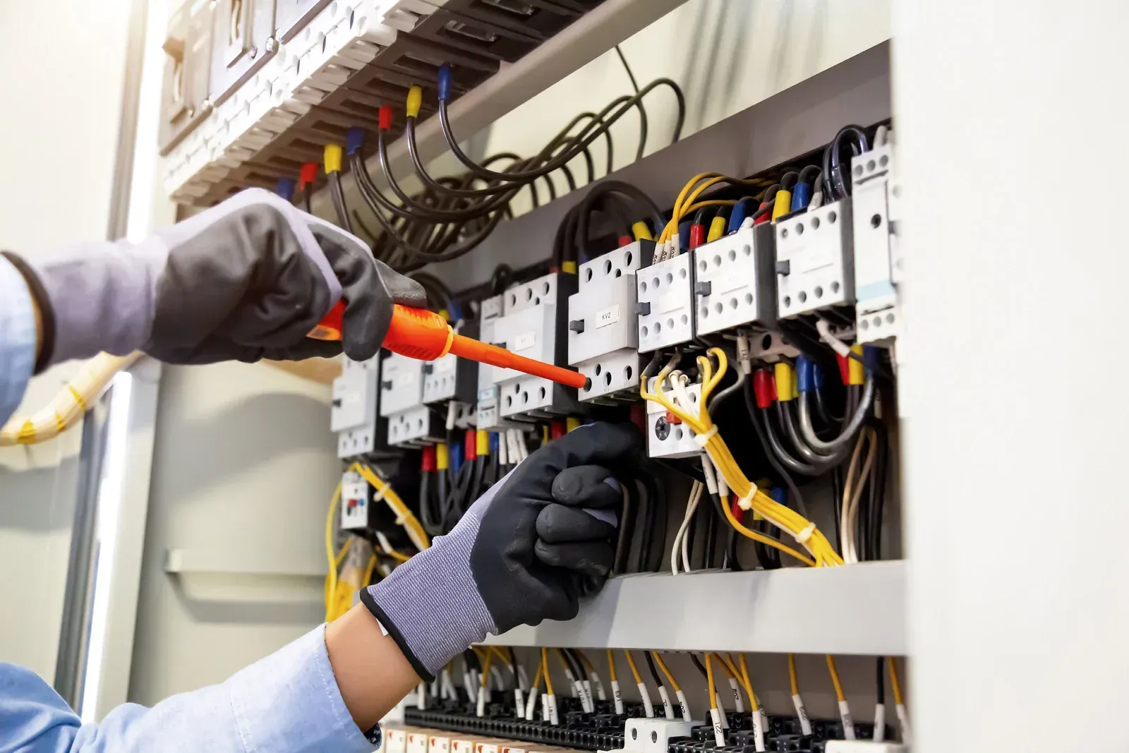 Technician wiring an electrical control panel with orange and yellow cables using a screwdriver