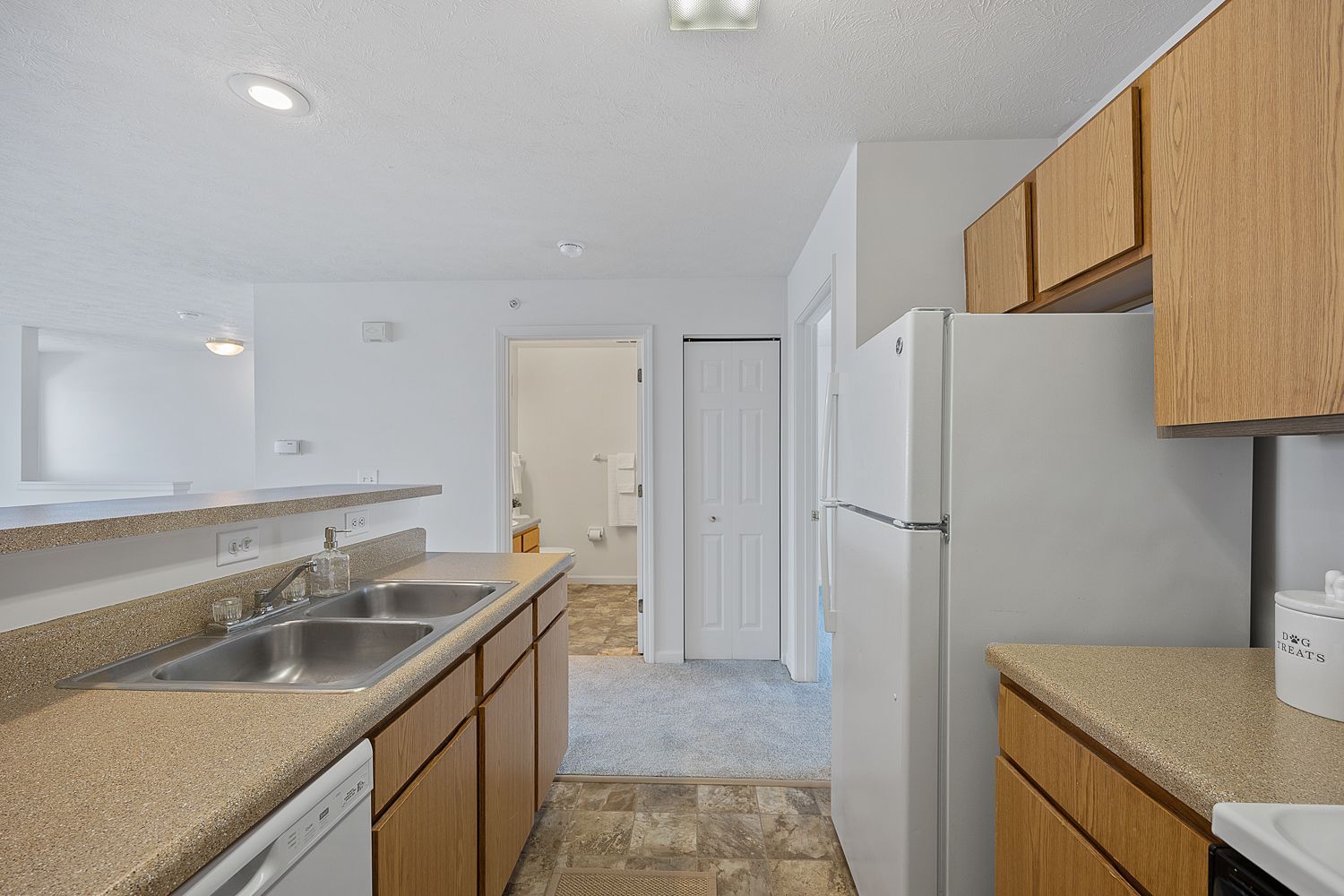 The Elm floor plan kitchen with refrigerator, wood cabinets, and breakfast bar counter.