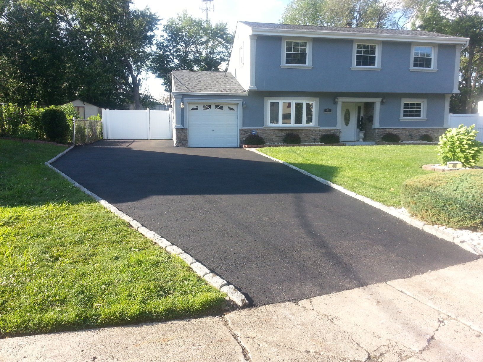 Residential building with freshly sealed asphalt driveway; orange cone near sewer.