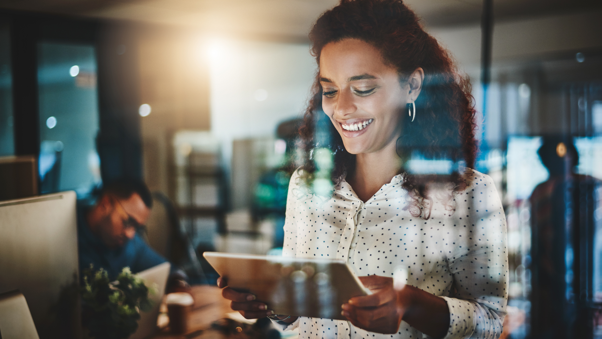 Woman smiling, holding tablet, working late in an office.