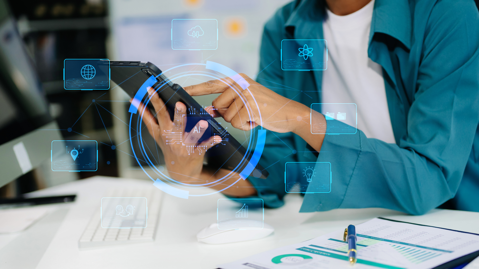 Person in blue jacket using a tablet, surrounded by digital interface icons at a desk.