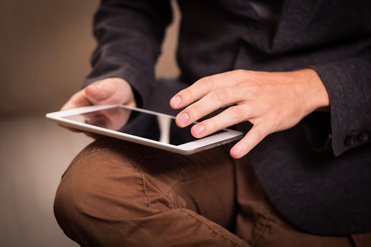 Person in a suit jacket and brown pants holding a tablet, touching the screen.