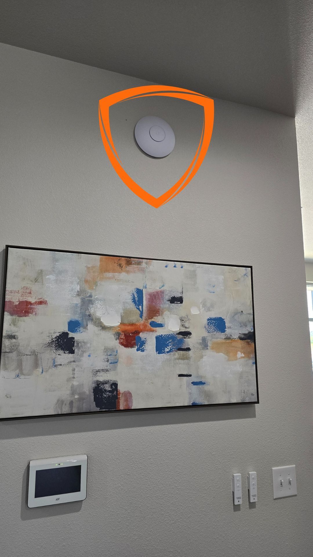 A painting is hanging on a wall next to a clock and a WiFi puck.