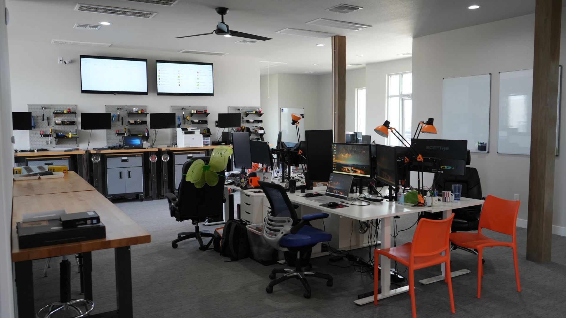 A large office with lots of desks and chairs and a ceiling fan.
