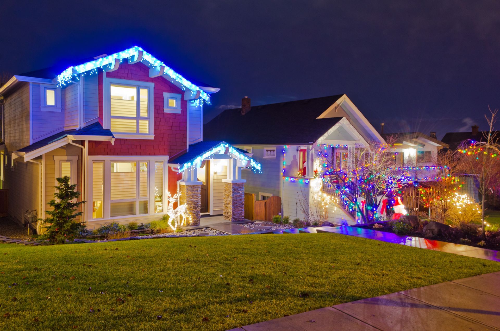 Houses decorated with blue and colorful Christmas lights at night.