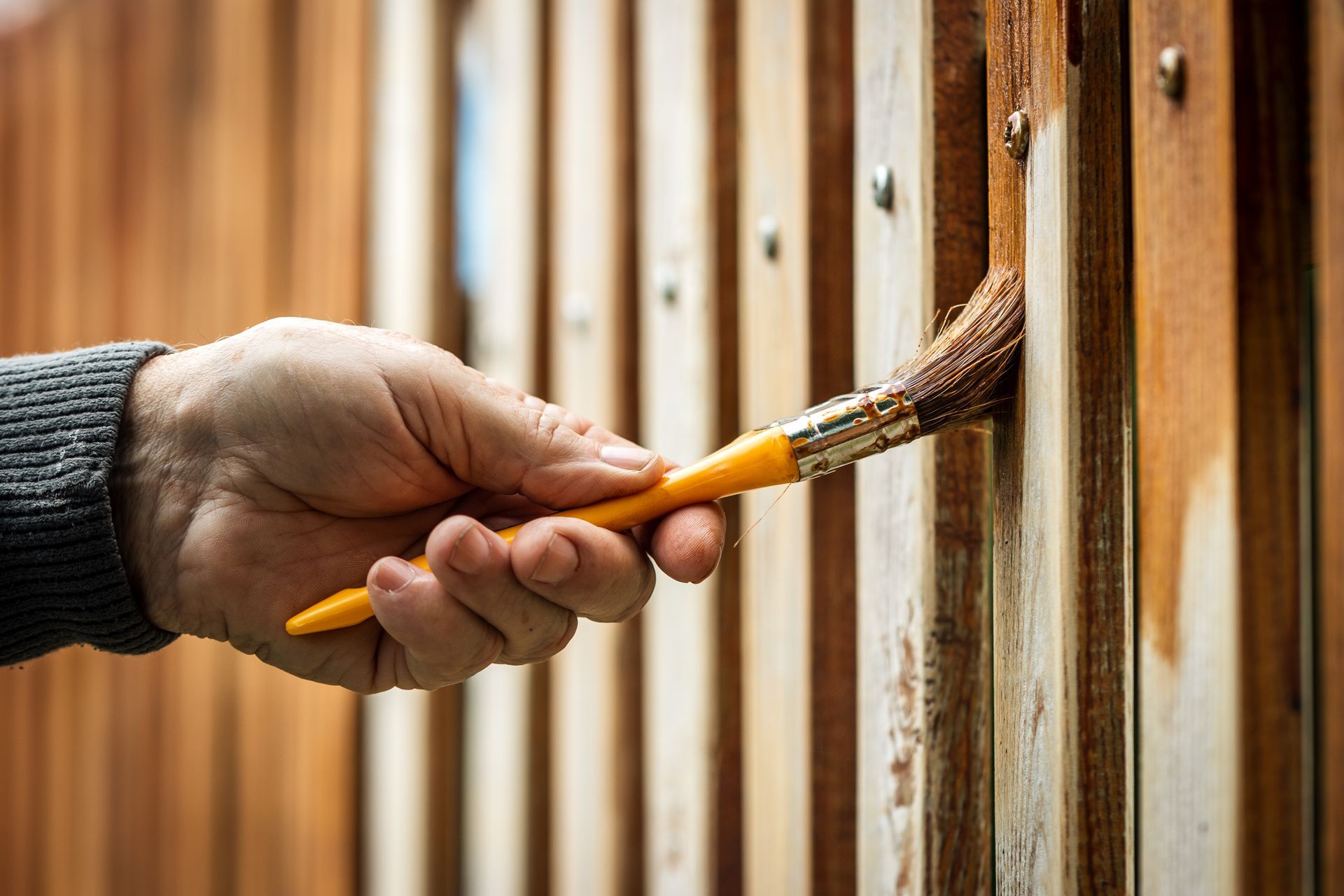 Hand painting a wooden fence with a brown stain.