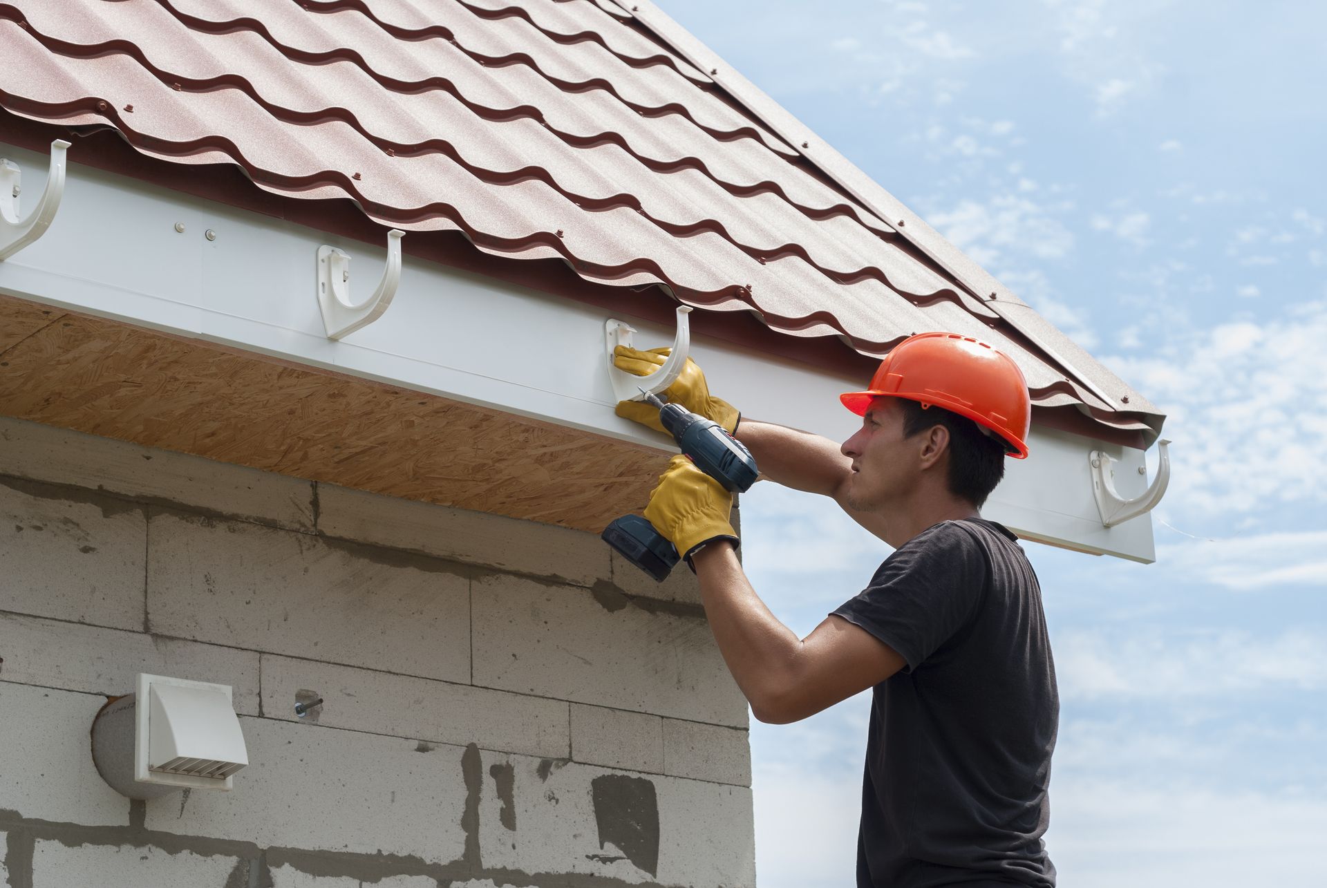 Man in hard hat installs a gutter on a brick building.