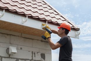 Man in hard hat installs a gutter on a brick building.