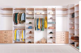 Walk-in closet with wooden shelves, drawers, and rods, filled with clothes, shoes, and accessories.