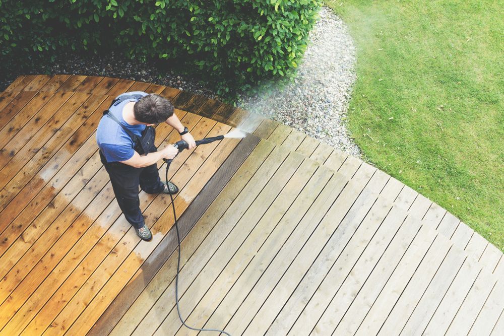 Man power washing a wooden deck outdoors.