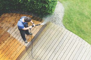 Man power washing wooden deck outdoors.