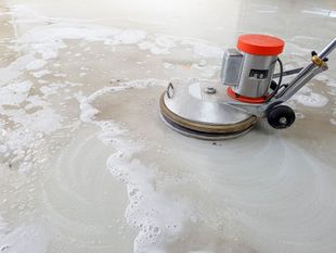 A floor buffer cleans a wet, soapy floor; machine is silver and orange.