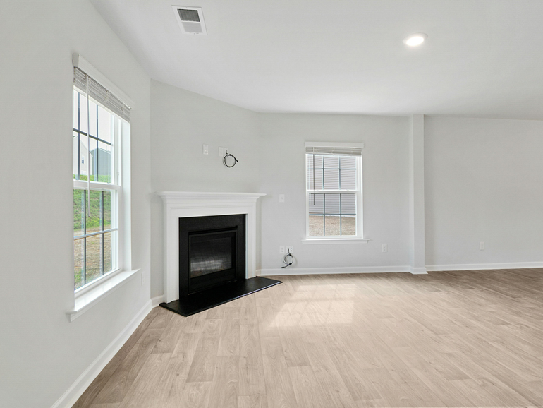 Empty living room with white walls, light wood floors, and a black fireplace mantel
