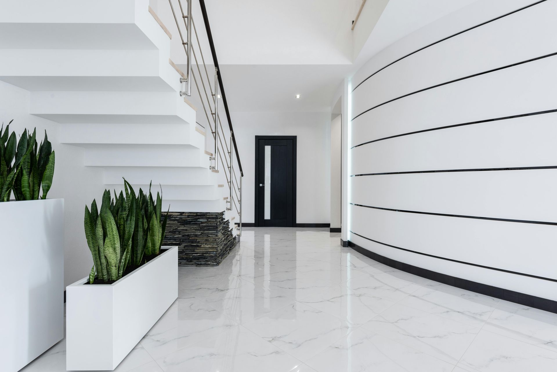 Bright modern lobby with white curved walls, stairs, potted plants, and a black door on glossy tile floor