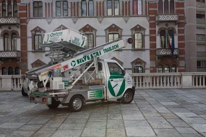 Un camion argentato e verde con una scala sul retro è parcheggiato davanti a un edificio